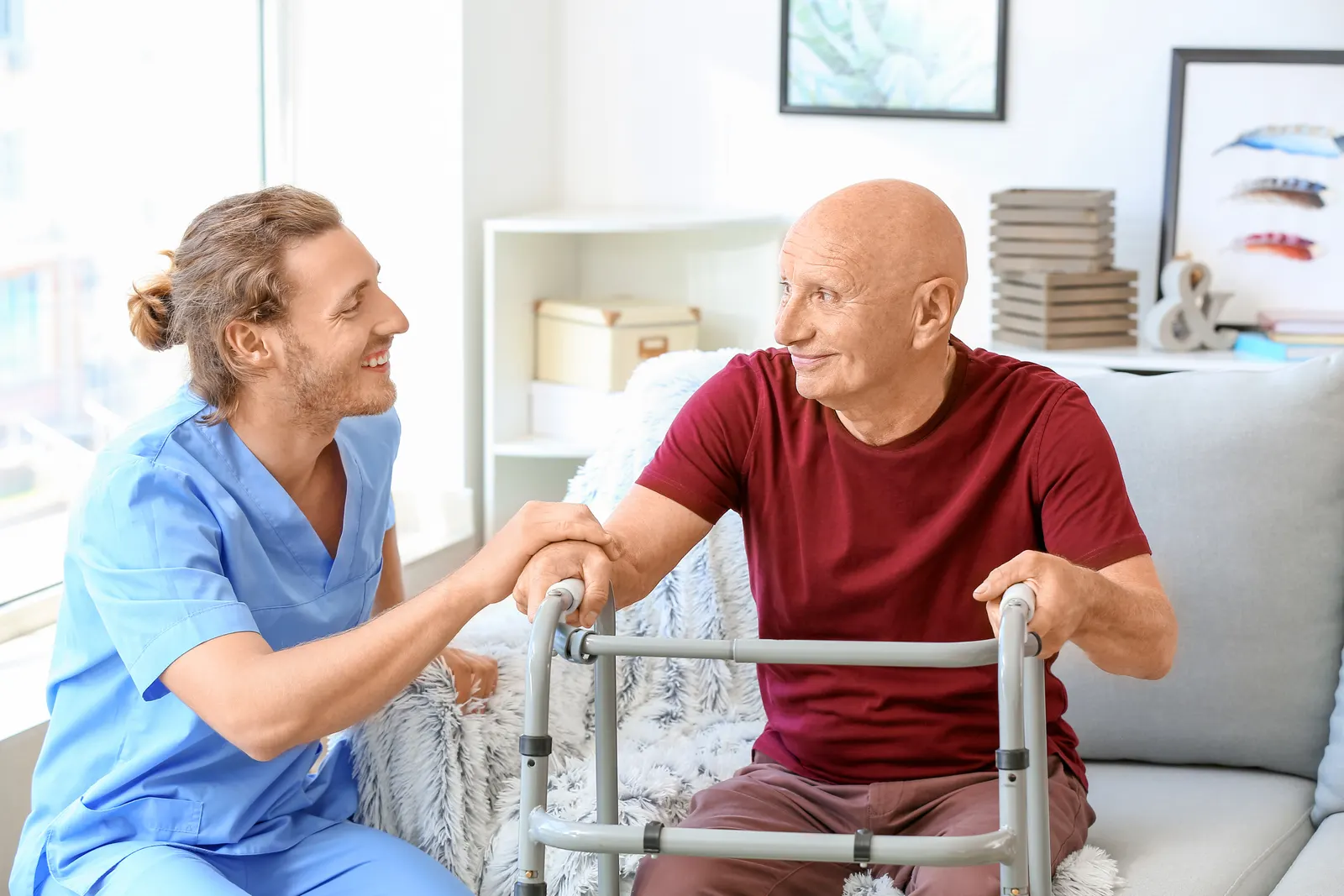 A therapist helping an older man stand from the couch with his walker