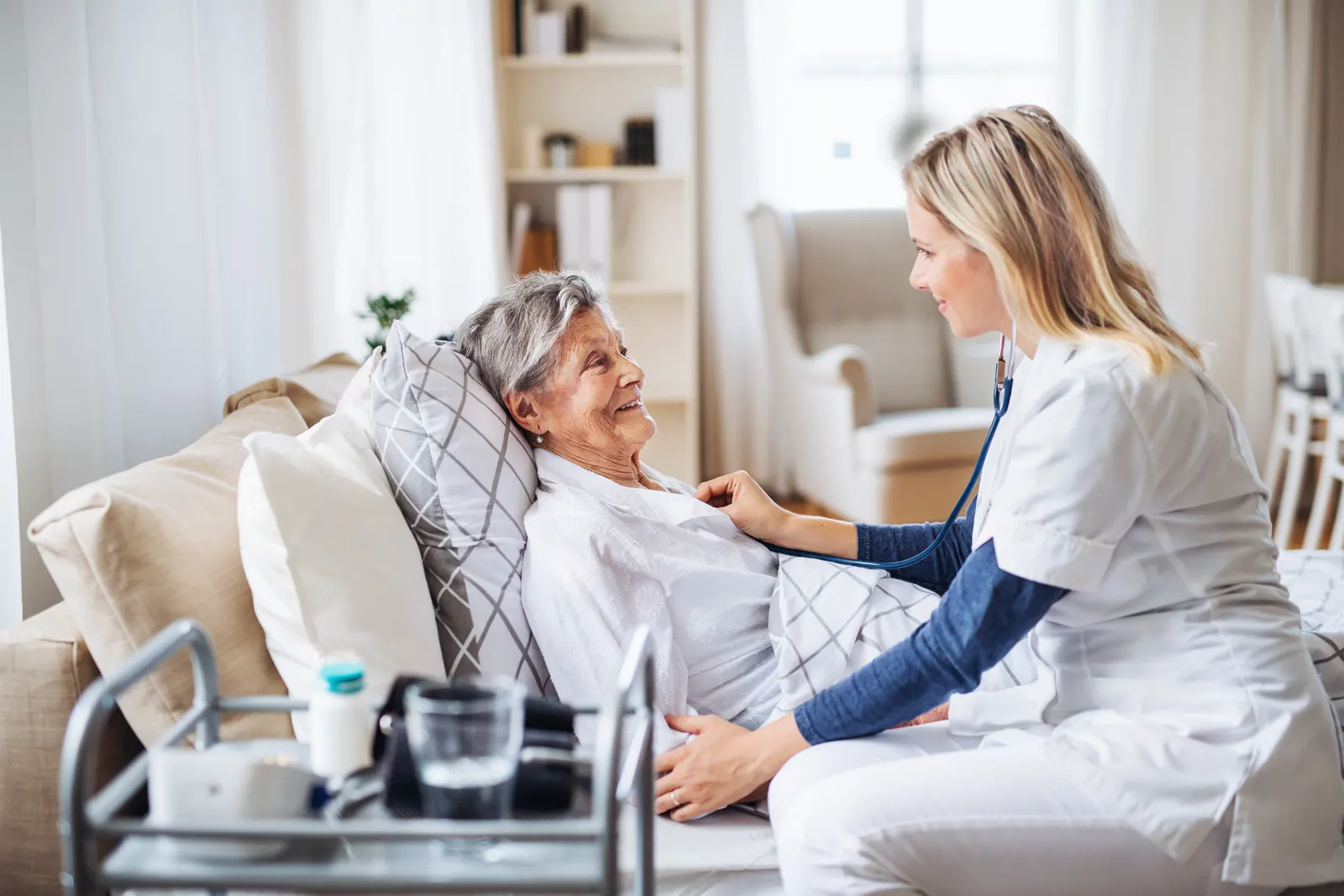 A nurse caring for an older woman resting on her sofa at home